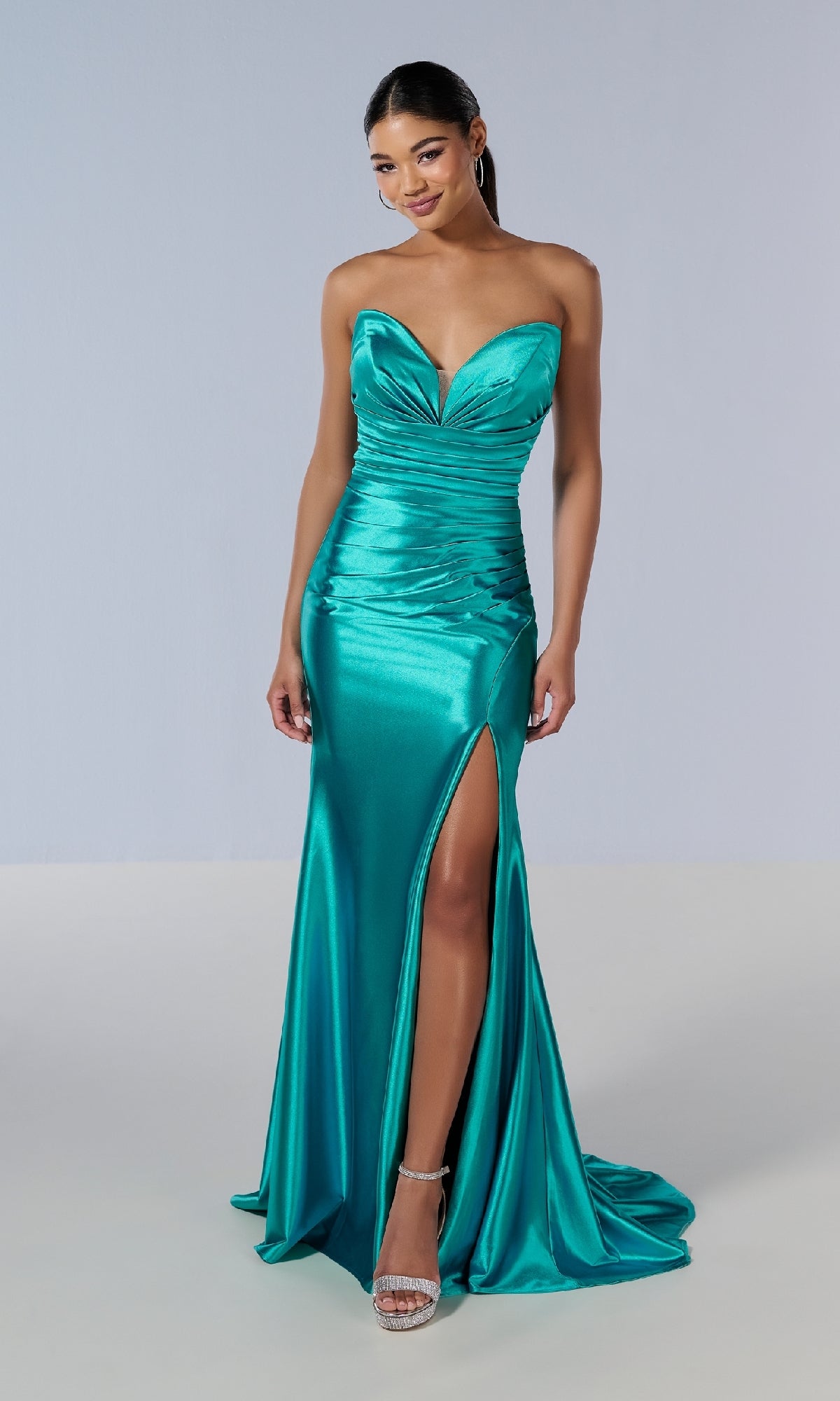 A woman stands against a plain background wearing the Tiffany 16182 long prom dress in teal satin, featuring a strapless sweetheart neckline, ruched bodice, thigh-high slit, and silver high-heeled sandals.